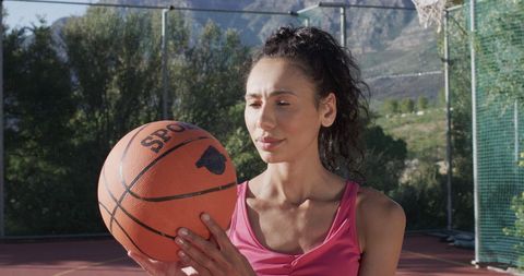 Female basketball player on outdoor sunny court holding ball