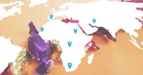 World map cutout with blue location pins over purple and gold candy foil wrappers concept