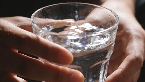 Closeup hands cradling glass of clear water with reflections and ripples
