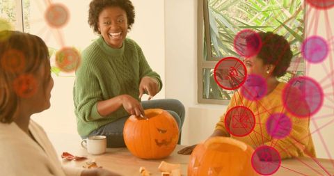Friends carving pumpkins and laughing during autumn gathering wearing cozy knit sweaters