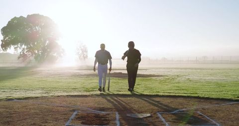 Early Morning Baseball Teammates Walking Toward Home Plate Carrying Bat and Helmet at Sunrise