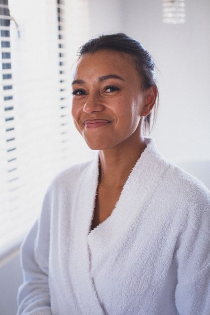Portrait of biracial woman wearing bathrobe looking to camera and smiling. staying at home in isolation during quarantine lockdown.