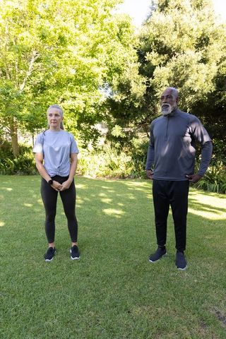 Outdoor fitness partners standing on lawn wearing sportswear and checking fitness tracker