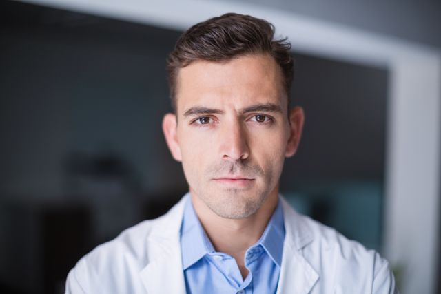 Male doctor wearing lab coat standing in hospital environment. Ideal for use in healthcare-related articles, medical websites, hospital brochures, and health awareness campaigns.