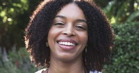 African american woman smiling in sunlit garden with curly hair and dangling earrings