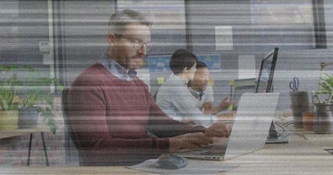 Focused professional typing at shared modern workspace with laptop, monitors, sticky notes