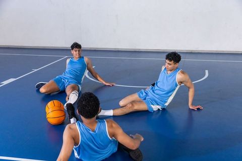 Teen Basketball Players in Blue Uniforms Stretching on Court