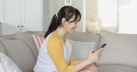 Smiling Woman Relaxing with Smartphone on Sofa