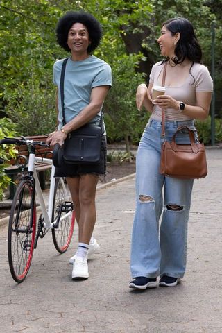 Diverse friends walking in park, pushing bicycle and holding coffee, urban lifestyle