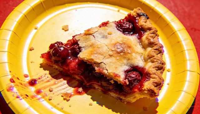 Rustic cherry pie slice shining on yellow paper plate with crumbly crust and glossy filling