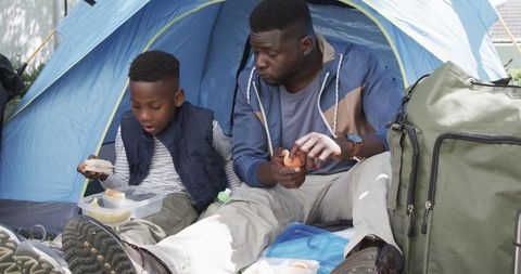 Father and Son Sharing Meal While Camping Inside Tent
