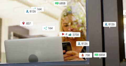 Woman checking smartphone in cafe with laptop showing social media notifications and engagement