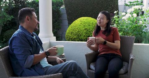 Asian couple sharing coffee and conversation on cozy porch with lush garden