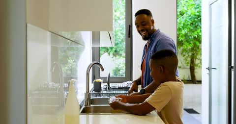 Father and Son Washing Dishes Together in Modern Kitchen
