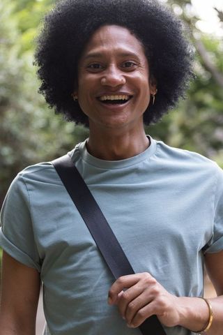 Smiling african american man adjusting crossbody strap in park, casual lifestyle portrait