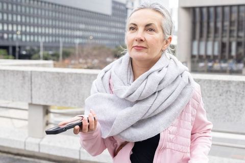 Mature woman holding smartphone looking thoughtful urban commute wearing scarf gray hair