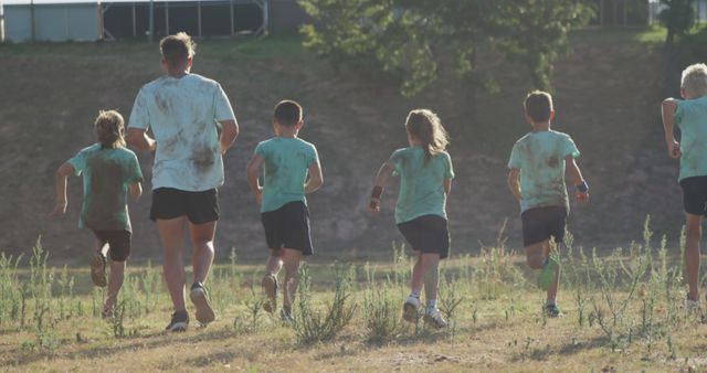Rear view of caucasian male instructor and children running across bootcamp training course. Fitness, childhood, friendship, challenge and healthy lifestyle.