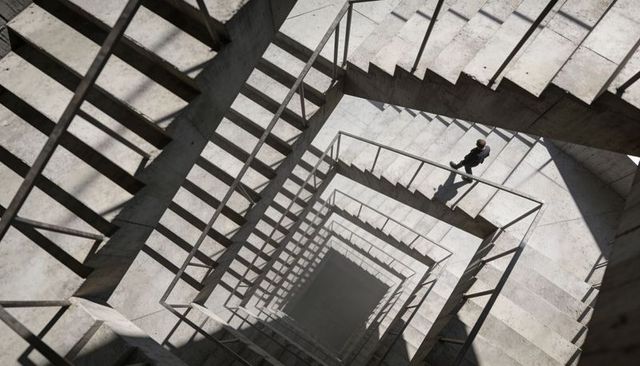 Top-down geometric concrete stairwell with person walking and dramatic long shadow