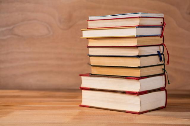 Several hardcover books stacked on a wooden table. Ideal for themes related to education, literature, studying, library resources, and the importance of reading. Useful for websites, brochures, and advertisements focusing on learning and knowledge.
