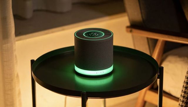 Compact smart speaker emitting green led ambient glow on round table in cozy living room