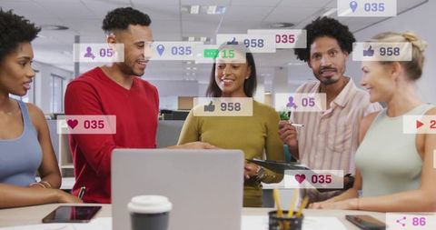 Diverse team collaborating at laptop with social media analytics overlays in open office