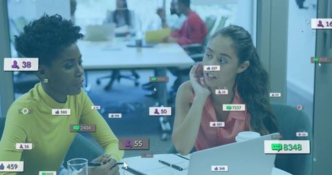 Two women collaborating at modern office desk with social media engagement overlays