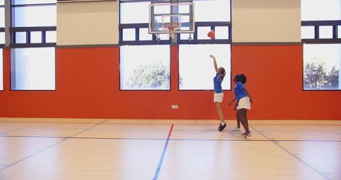 Young Female Basketball Players Shooting Hoop in Sunlit Gym
