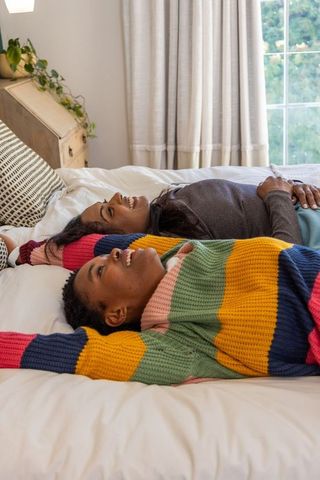 Relaxing together on bed, diverse female friends sharing cozy intimate bedroom moment