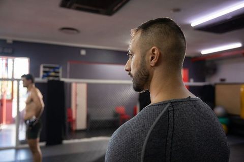 Mma coach observing fighter training in caged gym, focused coaching and sparring