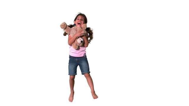 The image features a young girl joyfully playing with a teddy bear, creating a sense of carefree childhood happiness. Her spontaneous expression and playful energy make this image ideal for marketing materials focused on children's toys, clothing, or daycare environments. It can also be used in blog posts or social media content illustrating childhood joy, fun activities, or innocence.