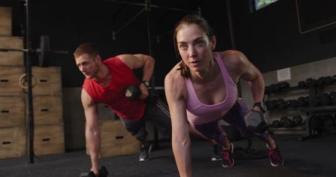 Focused Athletes Performing Dumbbell Push-Ups in Gym