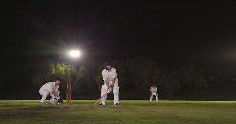 Night cricket match under floodlights with batsman at crease and wicketkeeper preparing