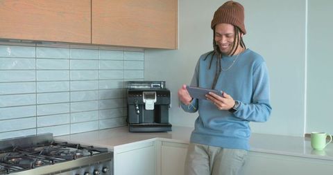 African american man smiling and reading tablet in modern kitchen near espresso machine