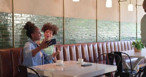 African american friends taking selfie over coffee in trendy leather-bench cafe interior