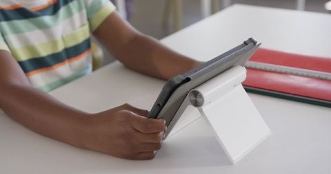 Child holding tablet on stand at study desk with binder and ruler for remote learning