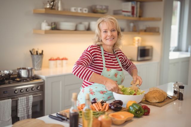 Portrait of smiling senior woman mixing vegetables salad in kitchen at home