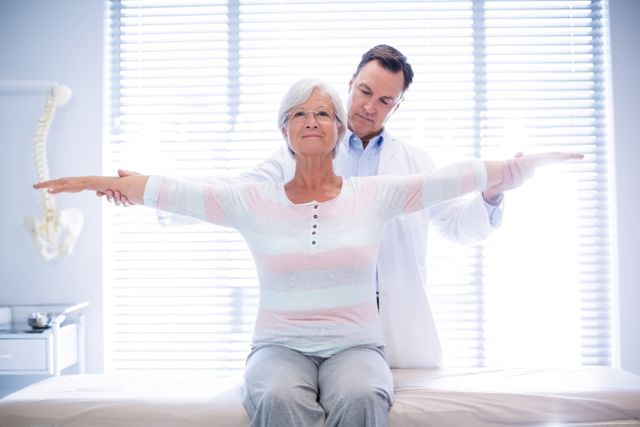 Senior woman receiving assistance from a physiotherapist with arm exercises in a clinic. Ideal for use in healthcare, rehabilitation, elderly care, and physical therapy contexts. Can be used in articles, brochures, and websites focused on senior health and wellness.