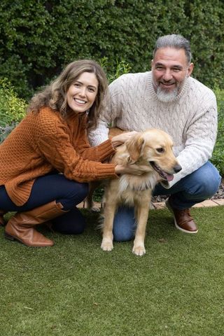 Smiling couple cuddling golden retriever in cozy cable-knit sweaters on backyard lawn