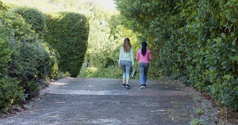 Women Walking on Hedgerow Path with Yoga Mat, Embracing Wellness Outdoors