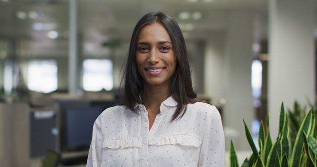 Image of happy biracial woman looking at camera in office. business professionals and working in office concept.