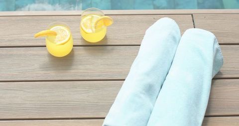 Light blue towels resting on poolside deck with citrus drinks and turquoise water