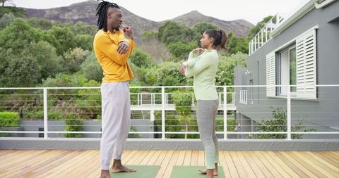 Couple stretching on terrace practicing morning yoga barefoot with scenic mountain view
