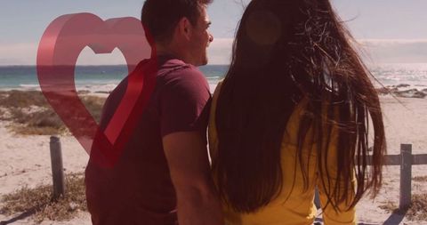 Romantic couple relaxing by the sea with heart graphic adjacent