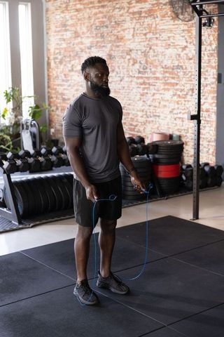 African american man holding blue jump rope in industrial gym for hiit training and cardio