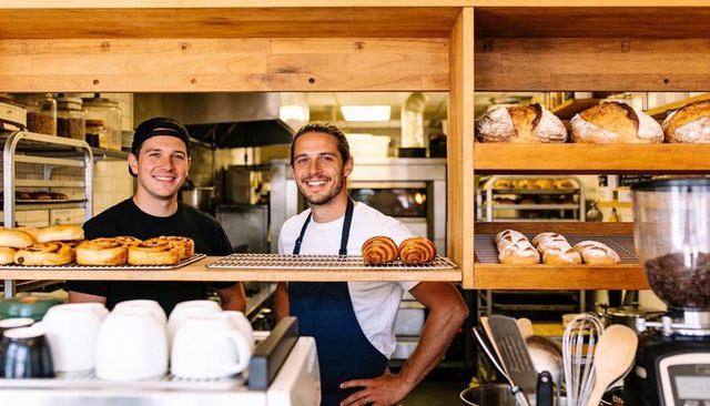 Smiling bakers arranging fresh croissants and artisan bread behind rustic bakery counter