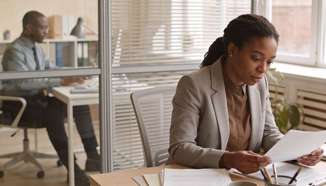 Focused businesswoman reviewing documents at modern office desk with colleague