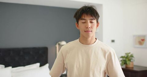 Young man standing with eyes closed relaxing in minimalist modern bedroom interior