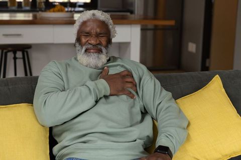 Senior african american man clutching chest on sofa experiencing sudden chest pain at home