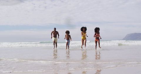Black family running through shallow surf on sunny beach with wet sand reflection