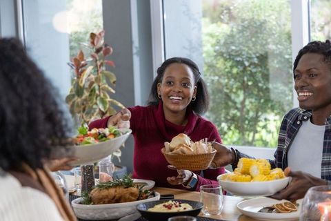 African american friends sharing meal and passing dishes around table, smiling together
